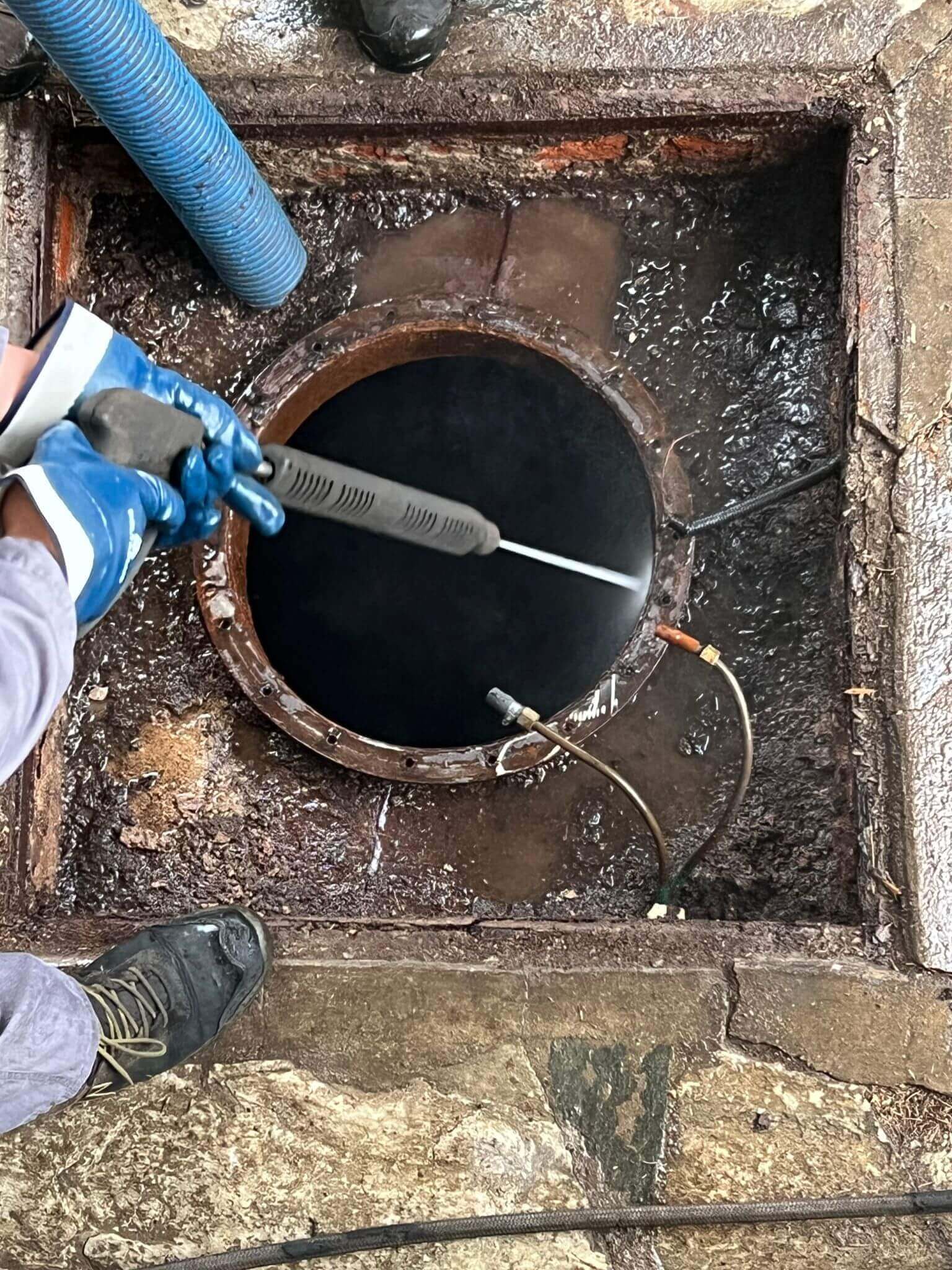 Worker cleaning sewer with power washer