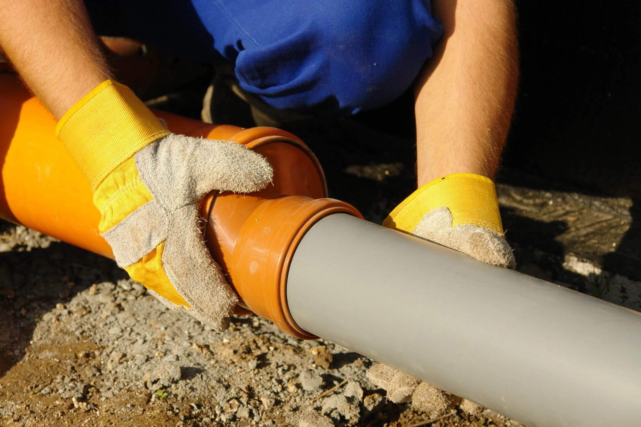 Worker fitting a gray pipe into an orange connector outdoors.